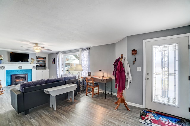 living room featuring baseboards, a ceiling fan, a tile fireplace, wood finished floors, and a textured ceiling