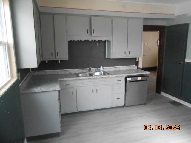 kitchen with dishwasher, gray cabinets, light wood finished floors, and a sink