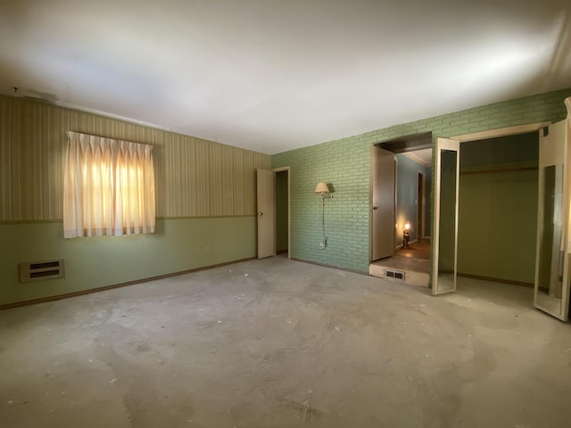 unfurnished bedroom with brick wall, concrete floors, visible vents, and baseboards