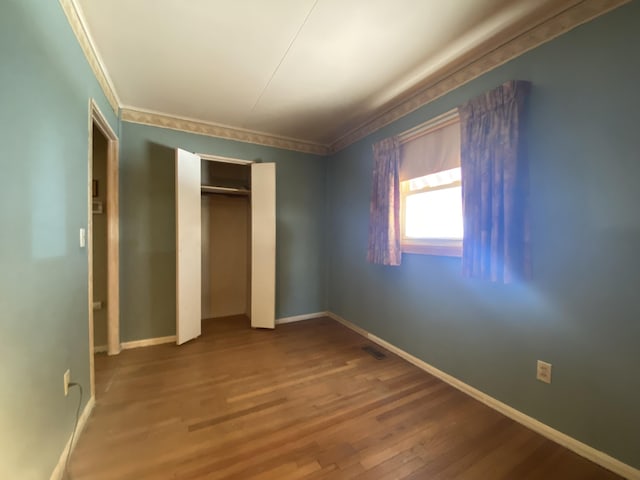 unfurnished bedroom with visible vents, crown molding, baseboards, and wood finished floors