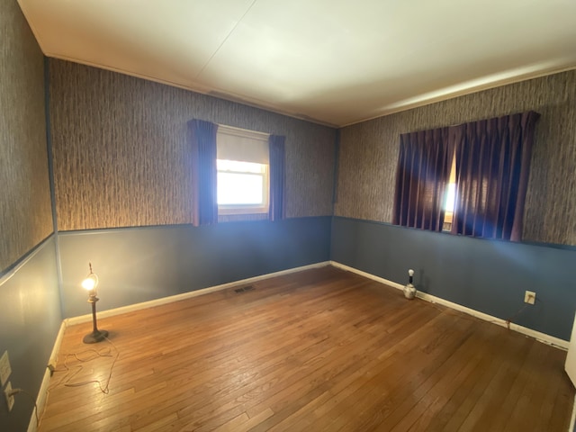 empty room featuring wood finished floors, visible vents, and baseboards