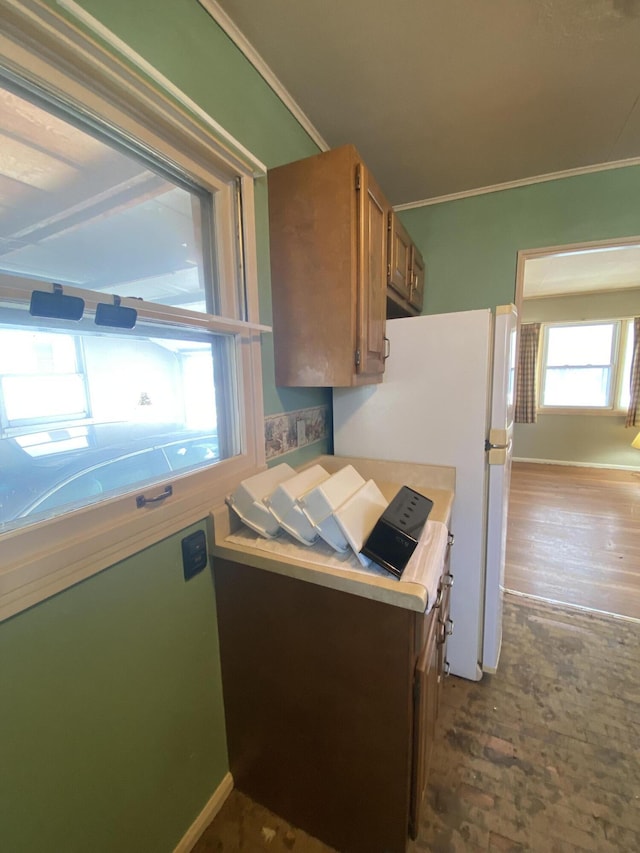 kitchen featuring baseboards, brown cabinetry, ornamental molding, freestanding refrigerator, and light countertops