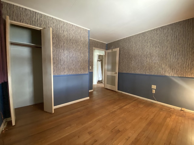 unfurnished bedroom featuring wallpapered walls, ornamental molding, wood finished floors, and a wainscoted wall