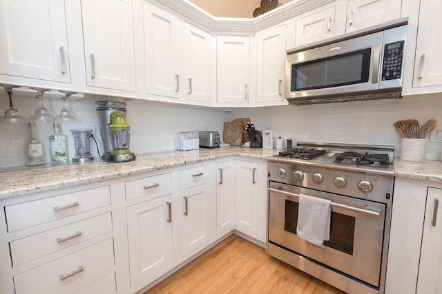 kitchen featuring appliances with stainless steel finishes, white cabinetry, backsplash, light stone counters, and light wood-type flooring