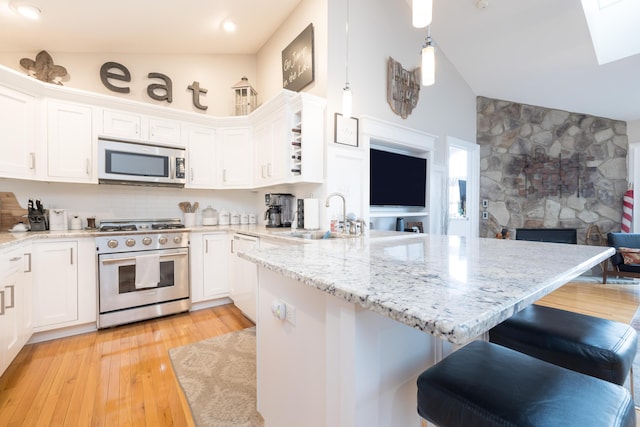 kitchen featuring sink, a breakfast bar, appliances with stainless steel finishes, white cabinets, and decorative light fixtures