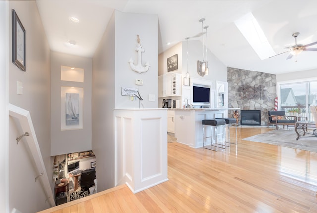 kitchen featuring a stone fireplace, a breakfast bar, a skylight, pendant lighting, and white cabinets