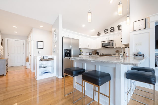 kitchen with appliances with stainless steel finishes, white cabinetry, lofted ceiling, hanging light fixtures, and kitchen peninsula