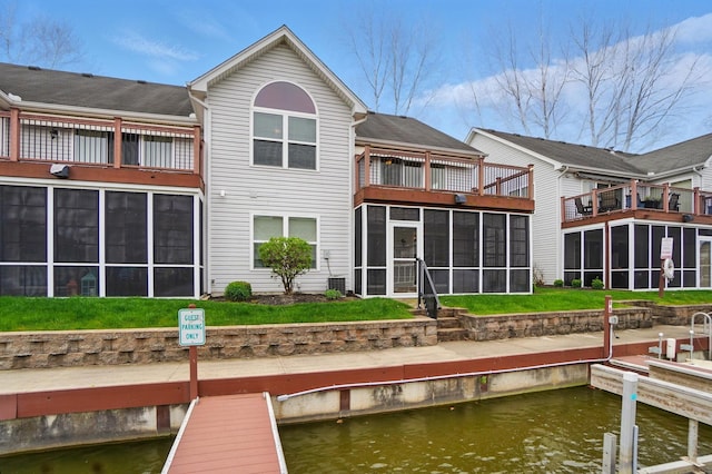 back of property with a balcony, cooling unit, a sunroom, a lawn, and a water view