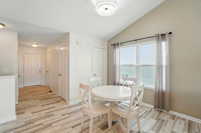 dining room with baseboards, light wood-style flooring, and vaulted ceiling