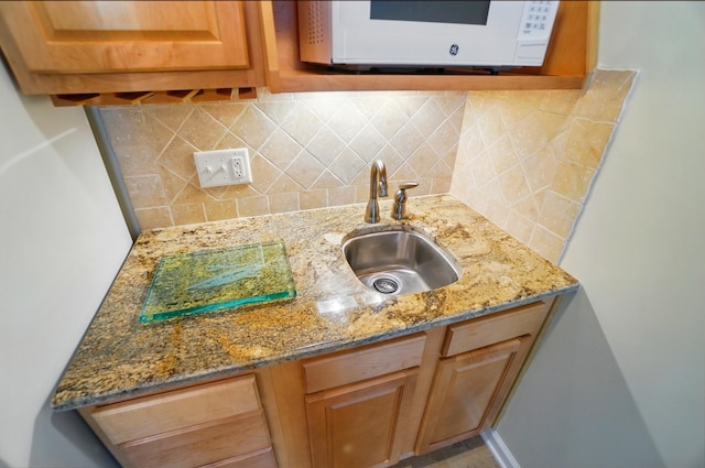kitchen featuring a sink, light stone counters, white microwave, and backsplash