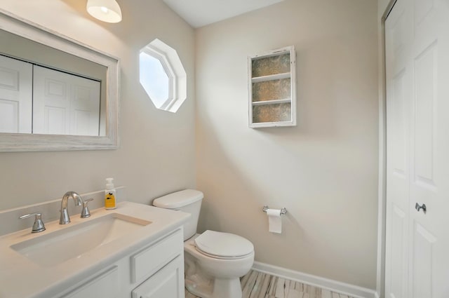 half bathroom featuring vanity, baseboards, a closet, and toilet