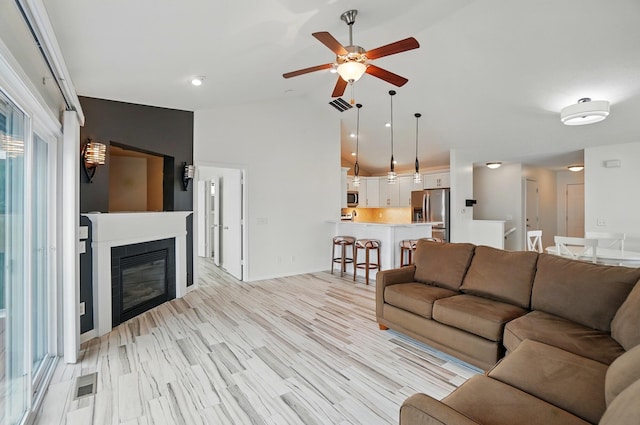 living room featuring ceiling fan, visible vents, a glass covered fireplace, and lofted ceiling