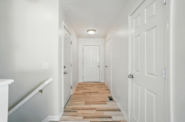 corridor with baseboards, light wood finished floors, and visible vents