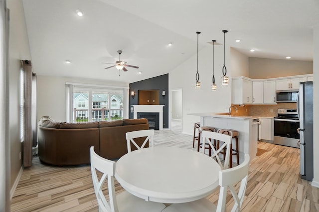 dining room with a glass covered fireplace, baseboards, ceiling fan, high vaulted ceiling, and light wood-style flooring