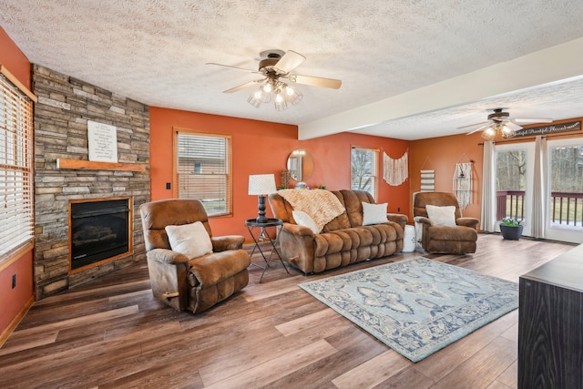 living room with hardwood / wood-style flooring, ceiling fan, a fireplace, and a textured ceiling