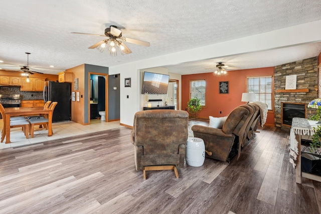 living room featuring light hardwood / wood-style flooring, a textured ceiling, a fireplace, and ceiling fan