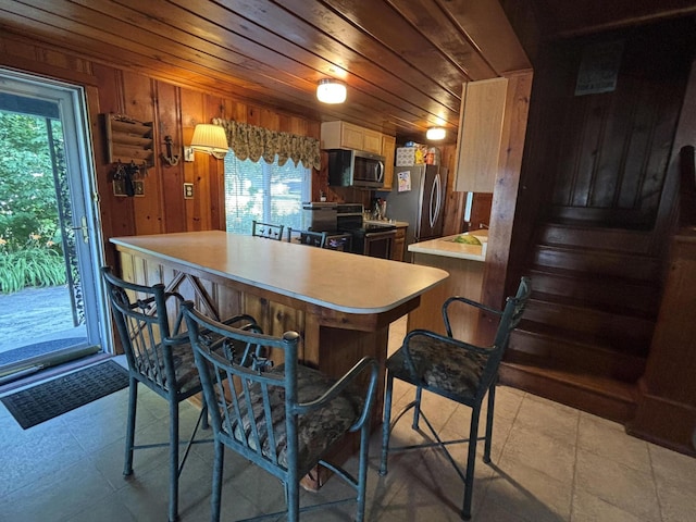 9029 Maple St, Huntsville, OH 43324 - kitchen with appliances with stainless steel finishes, light countertops, wood walls, wooden ceiling, and a kitchen bar