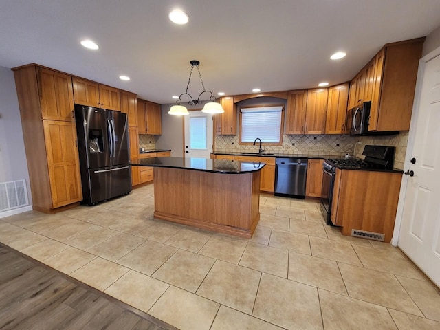 kitchen with dark countertops, visible vents, a center island, appliances with stainless steel finishes, and a sink