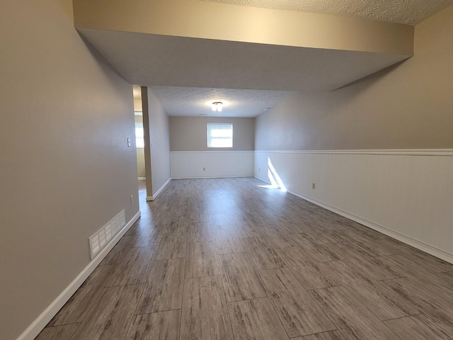 empty room featuring wood finished floors, wainscoting, visible vents, and a textured ceiling