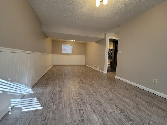 basement featuring visible vents, a wainscoted wall, a textured ceiling, and wood finished floors