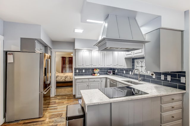 kitchen with black electric stovetop, a peninsula, a sink, wall chimney exhaust hood, and stainless steel fridge