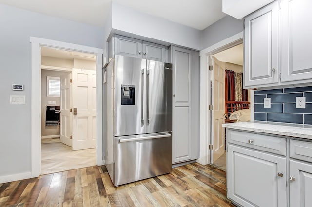 kitchen with light stone counters, stainless steel refrigerator with ice dispenser, gray cabinets, backsplash, and light wood-style floors