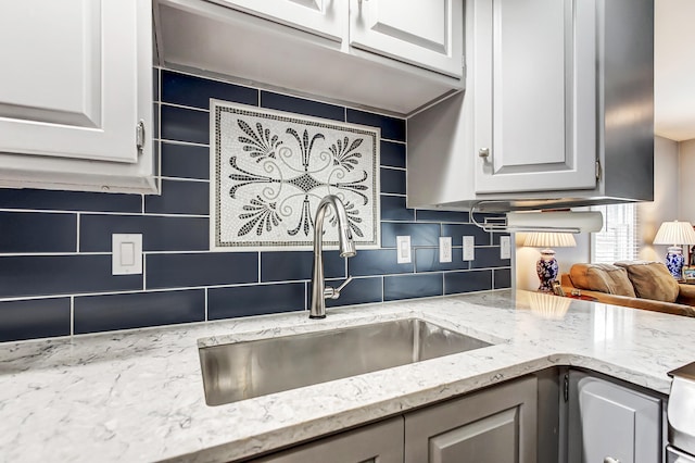 kitchen with tasteful backsplash, a sink, white cabinetry, and light stone countertops