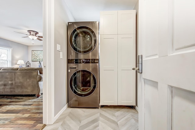 laundry area featuring cabinet space, parquet flooring, baseboards, a ceiling fan, and stacked washing maching and dryer