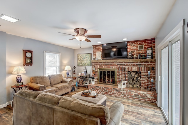 living area featuring a ceiling fan, a fireplace, baseboards, and wood finished floors