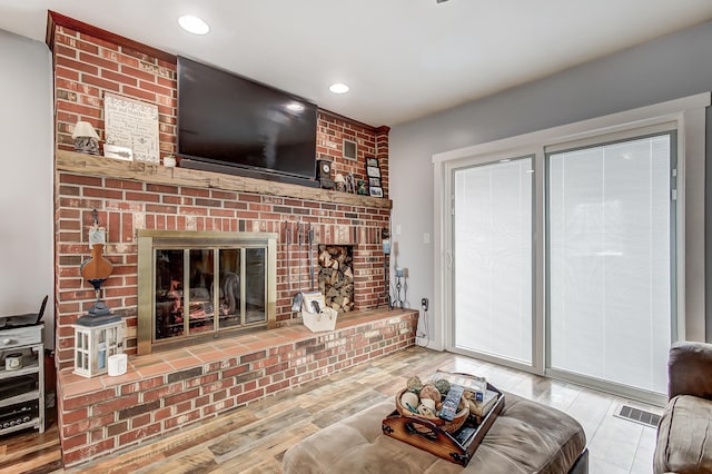 living room featuring a brick fireplace, visible vents, wood finished floors, and recessed lighting