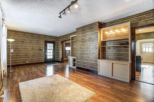 unfurnished room with wooden walls, dark hardwood / wood-style floors, a textured ceiling, and rail lighting