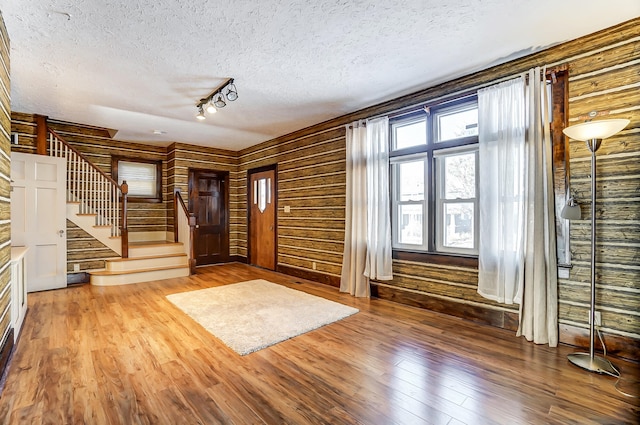 entrance foyer with hardwood / wood-style flooring, track lighting, a textured ceiling, and wood walls