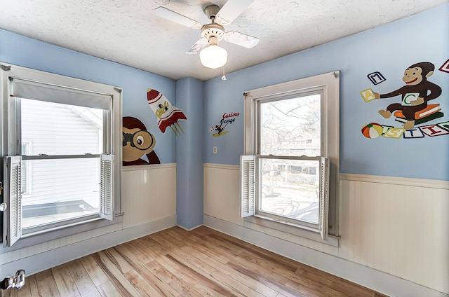 doorway with ceiling fan, light hardwood / wood-style flooring, and a textured ceiling