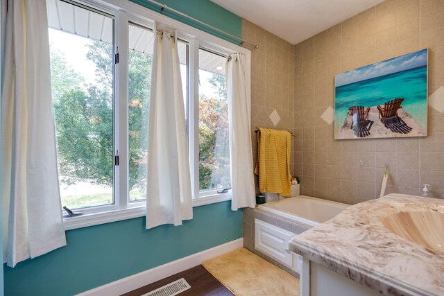 bathroom featuring vanity, wood-type flooring, tile walls, and a bathing tub