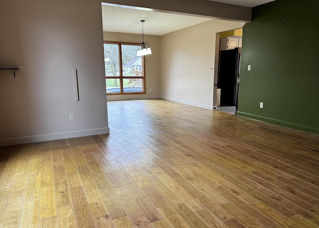 spare room featuring beam ceiling, a chandelier, and light wood-type flooring