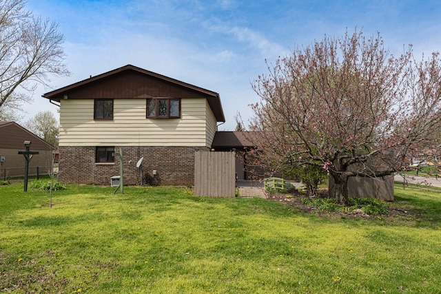 back of house with brick siding, a lawn, and fence