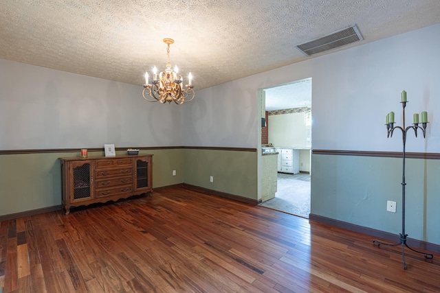 unfurnished dining area featuring wood finished floors, a textured ceiling, a chandelier, baseboards, and visible vents