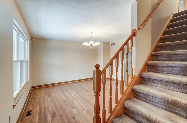 stairs featuring an inviting chandelier, visible vents, baseboards, and wood finished floors