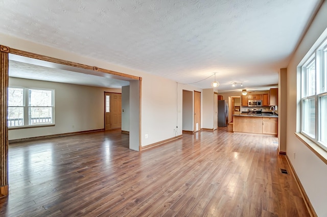 unfurnished living room with a textured ceiling, baseboards, a sink, and light wood-style floors