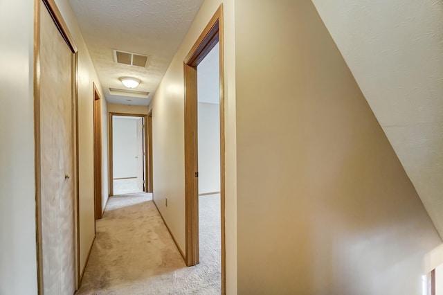 corridor featuring visible vents, a textured ceiling, and light colored carpet