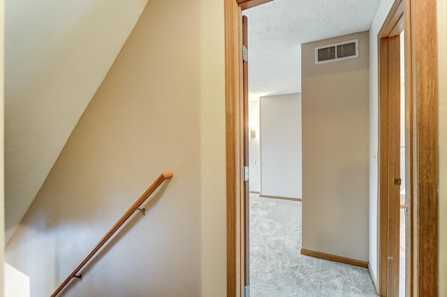 corridor with a textured ceiling, light colored carpet, an upstairs landing, baseboards, and visible vents