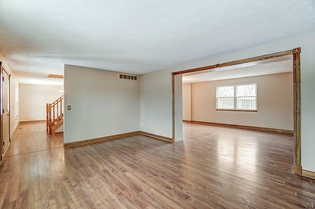 unfurnished room featuring stairs, light wood finished floors, visible vents, and baseboards