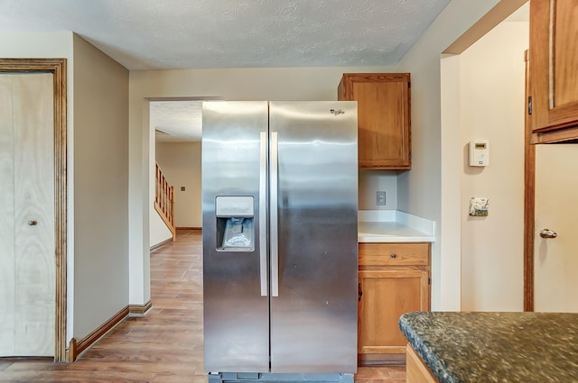 kitchen with dark countertops, stainless steel refrigerator with ice dispenser, light wood-style flooring, and brown cabinets