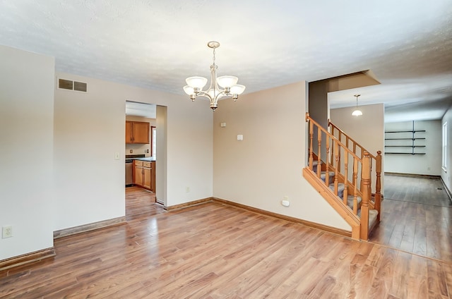 empty room featuring light wood-style flooring, visible vents, baseboards, stairway, and an inviting chandelier