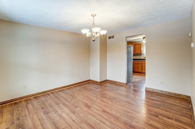 spare room with baseboards, visible vents, a textured ceiling, light wood-style floors, and a chandelier