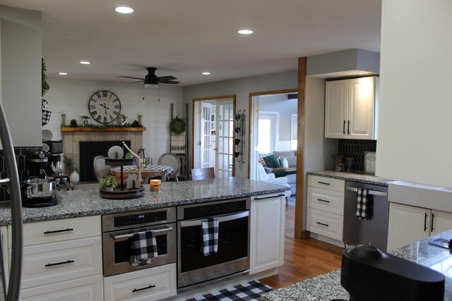 kitchen with dishwashing machine, a tile fireplace, wood finished floors, and stainless steel oven