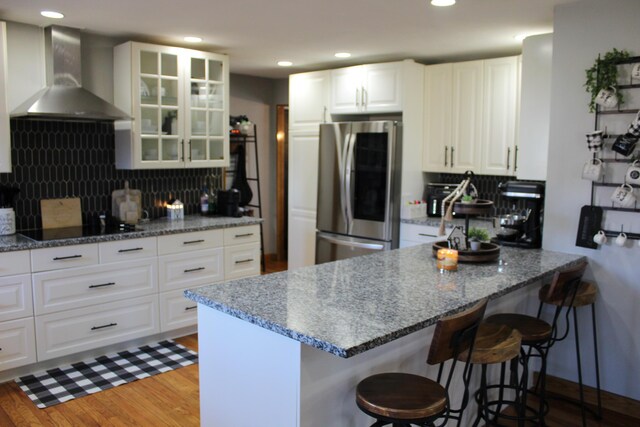 kitchen with smart refrigerator, light wood-style floors, a peninsula, wall chimney range hood, and black electric cooktop