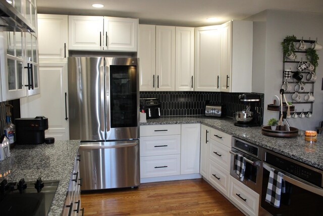 kitchen featuring stone countertops, tasteful backsplash, wood finished floors, white cabinetry, and appliances with stainless steel finishes