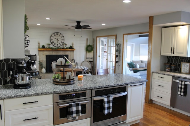 kitchen featuring decorative backsplash, a fireplace, light wood-style floors, white cabinets, and stainless steel appliances