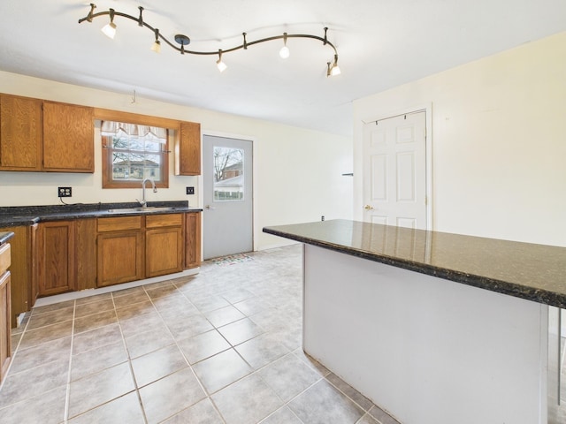 kitchen with dark stone countertops, brown cabinets, light tile patterned floors, and a sink